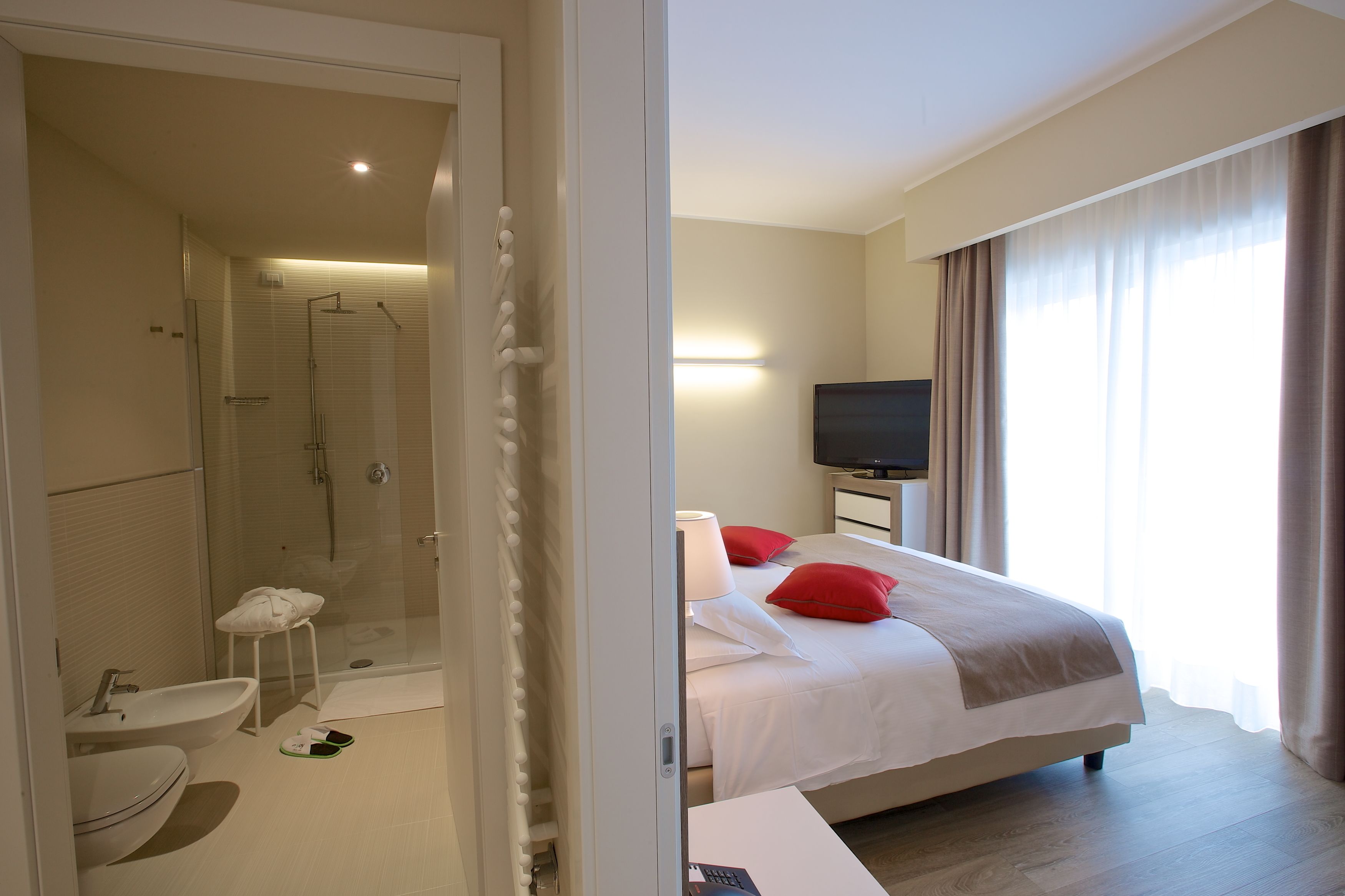 Een hotelkamer met douche, toilet, wastafel, bed, televisie en uitzicht op de omgeving.