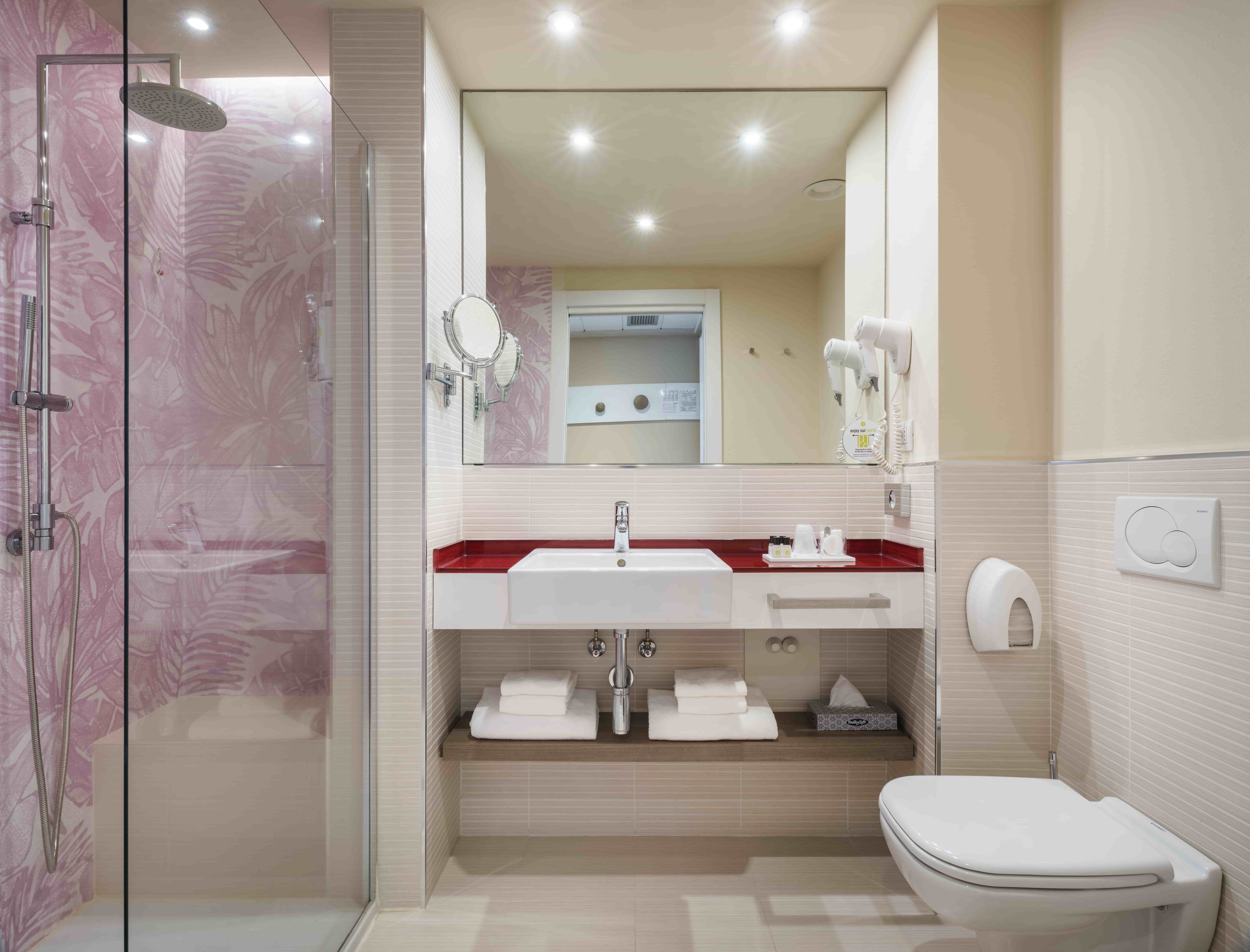 Une salle de bain moderne avec une douche à parois de verre, un lavabo blanc doté d’un plan de toilette rouge et des toilettes.