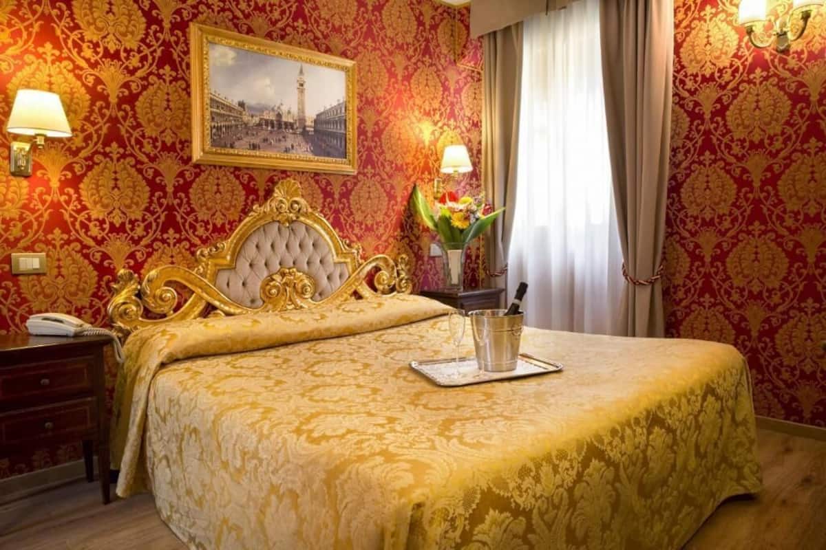 Una habitación de hotel con una cama grande, un llamativo cabecero dorado y un papel tapiz rojo con estampado.