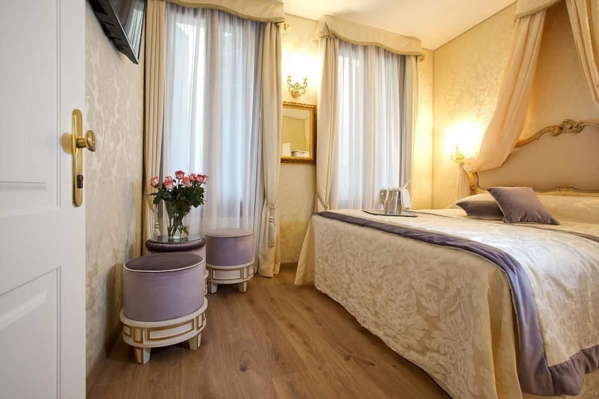 Un dormitorio con cama, tocador con espejo y ventana con cortinas.