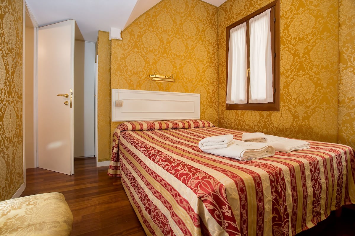 Una habitación de hotel con una cama, una mesita de noche, una ventana con cortinas y una puerta.