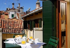 A table set for breakfast with a view of terracotta-tiled rooftops and a green door. - Residenza Goldoni (Venice)