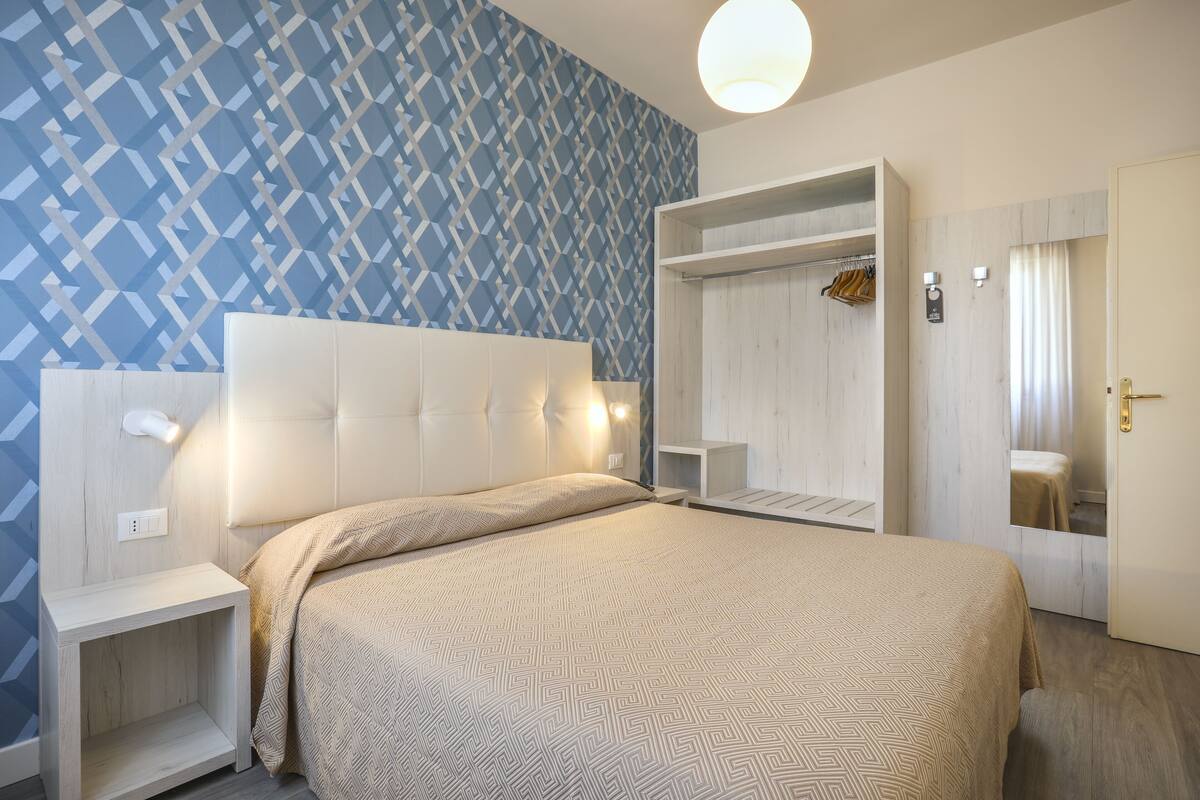 Et hotelværelse med en stor seng, et garderobeskab, et spejl og et natbord.