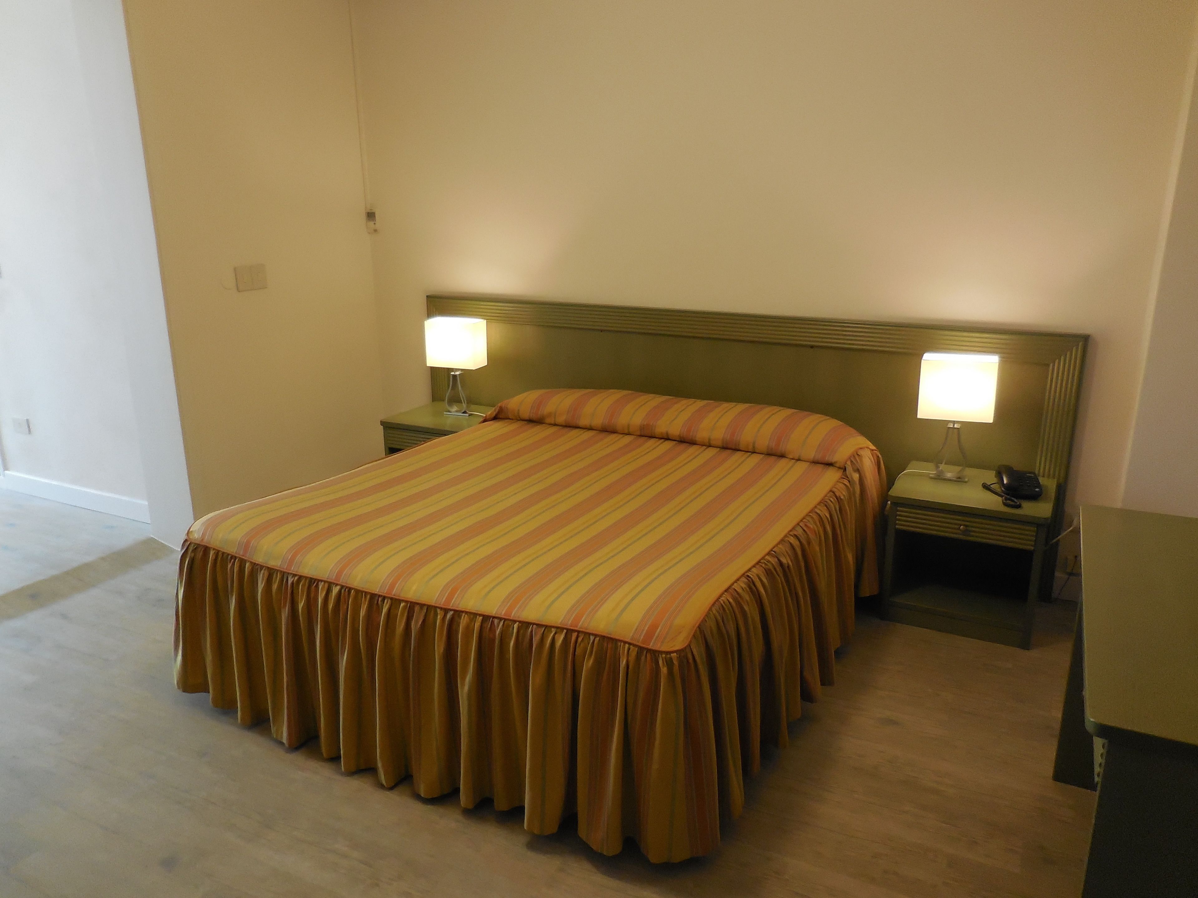 Ein Hotelzimmer mit einem großen Bett, zwei Nachttischen mit Lampen und einem Beistelltischchen mit Telefon.