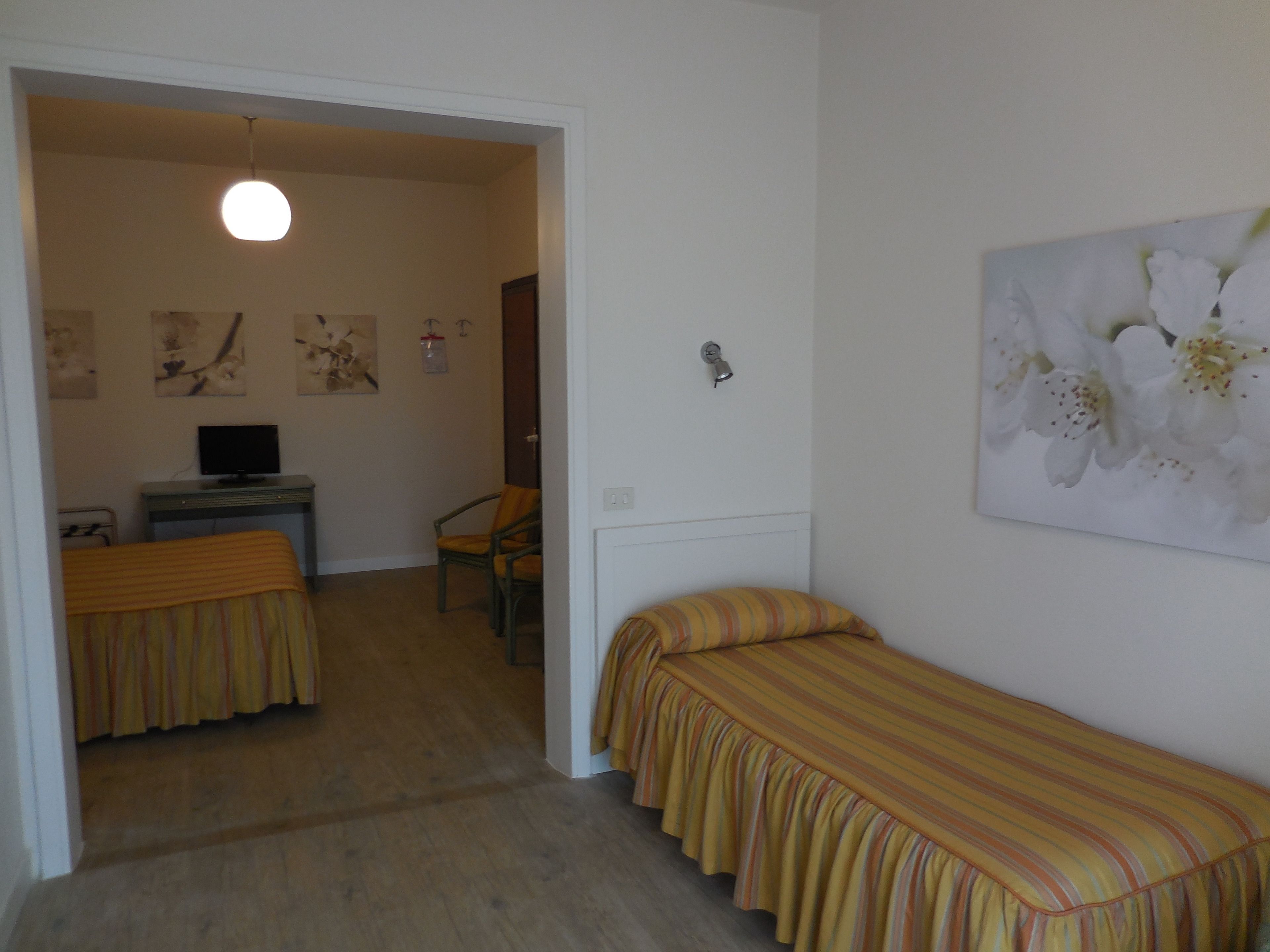 Een slaapkamer met een bed, een stoel, een bureau met een computer en een schilderij aan de muur.