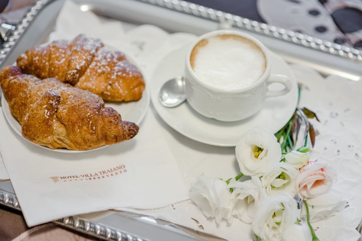 Ein Tablett mit Croissants, einer Kaffeetasse und einem Blumenstrauß.