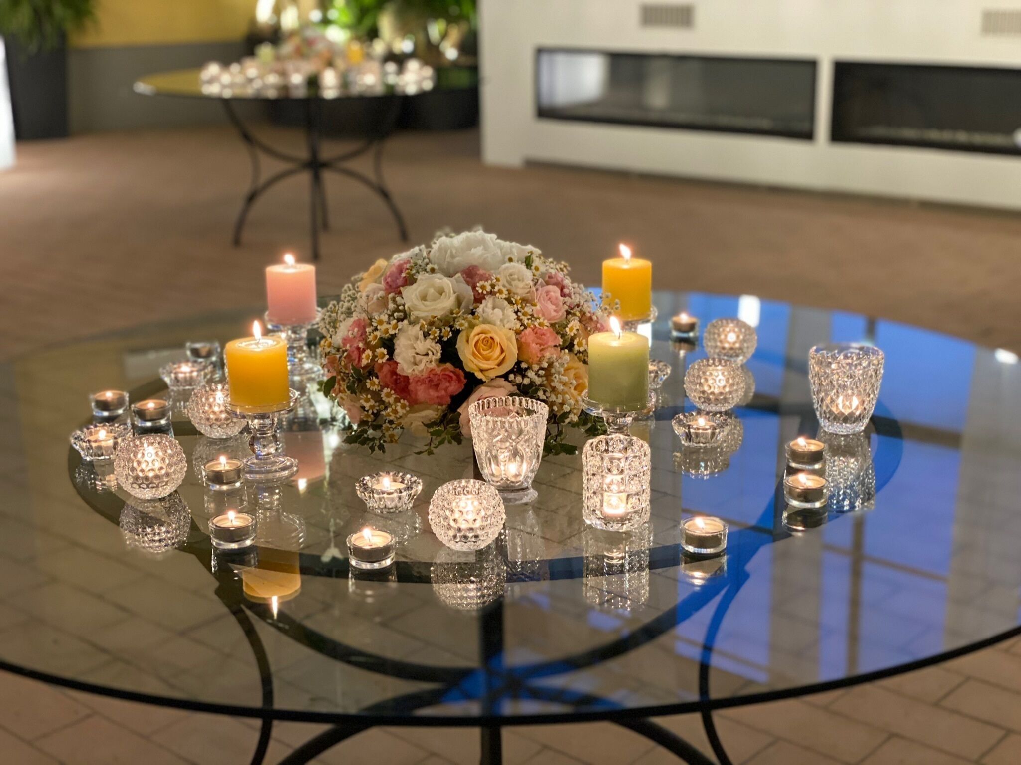 A round glass table with candles and a floral centerpiece.