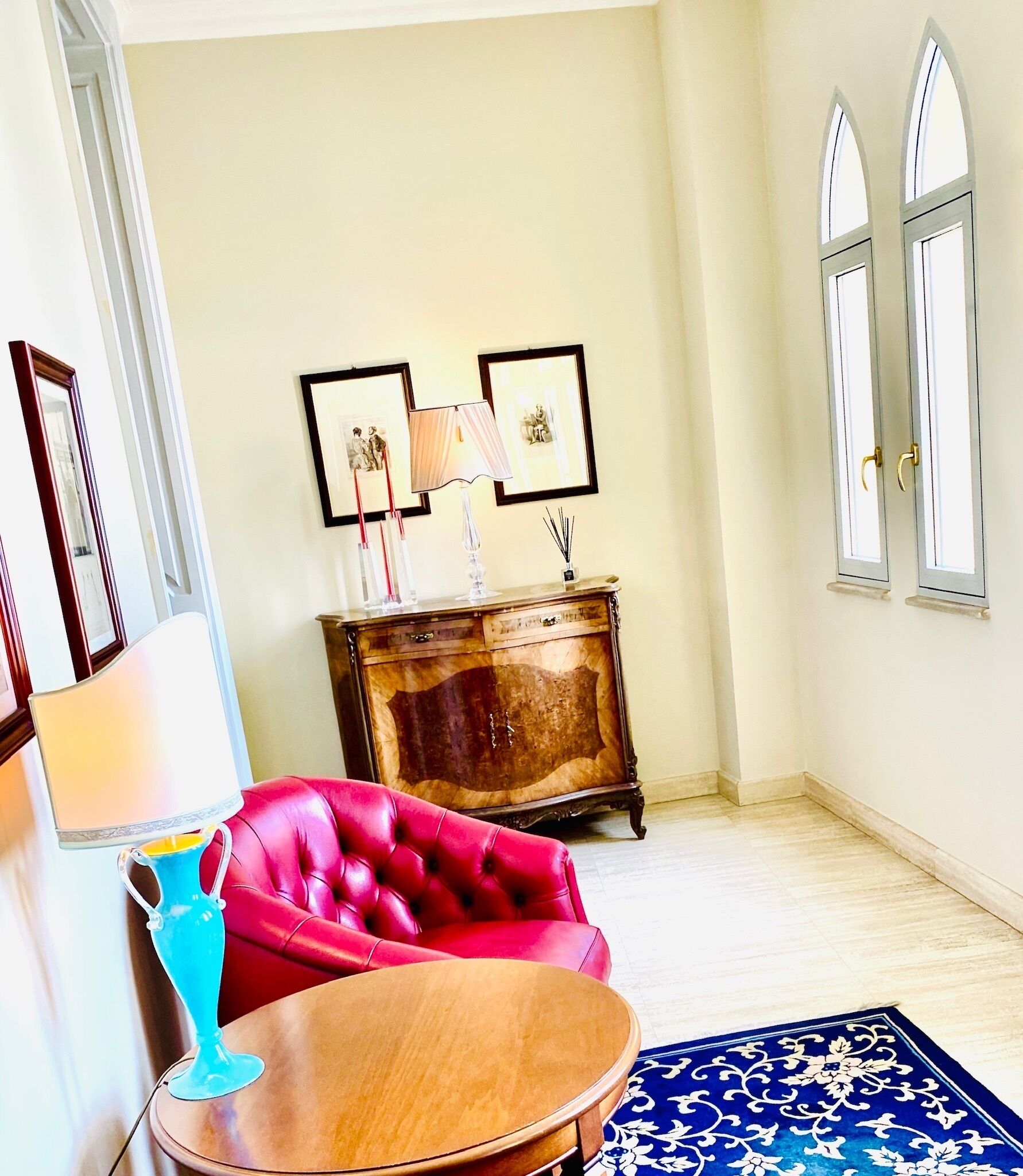 A room with a red leather sofa, a wooden side table, a blue vase, a wooden cabinet with pictures, and a blue patterned rug.