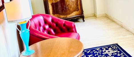 A room with a red leather sofa, a wooden side table, a blue vase, a wooden cabinet with pictures, and a blue patterned rug.