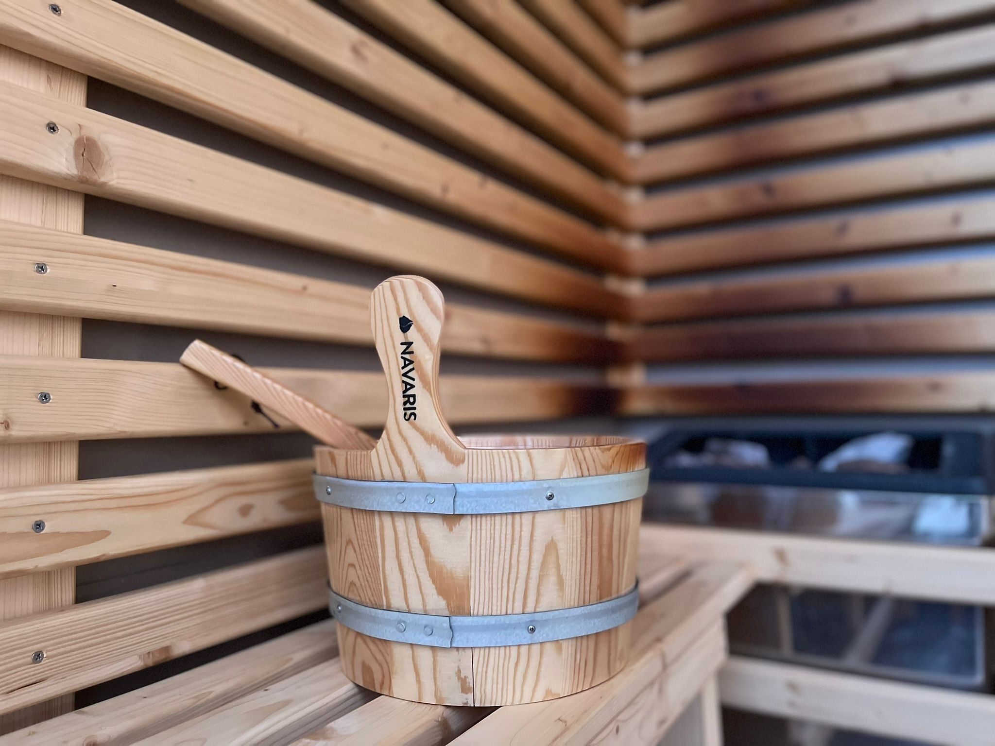 A wooden bucket with a metal band and a handle labeled "NAVARIS" against a backdrop of wooden slats.
