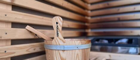 A wooden bucket with a metal band and a handle labeled "NAVARIS" against a backdrop of wooden slats.
