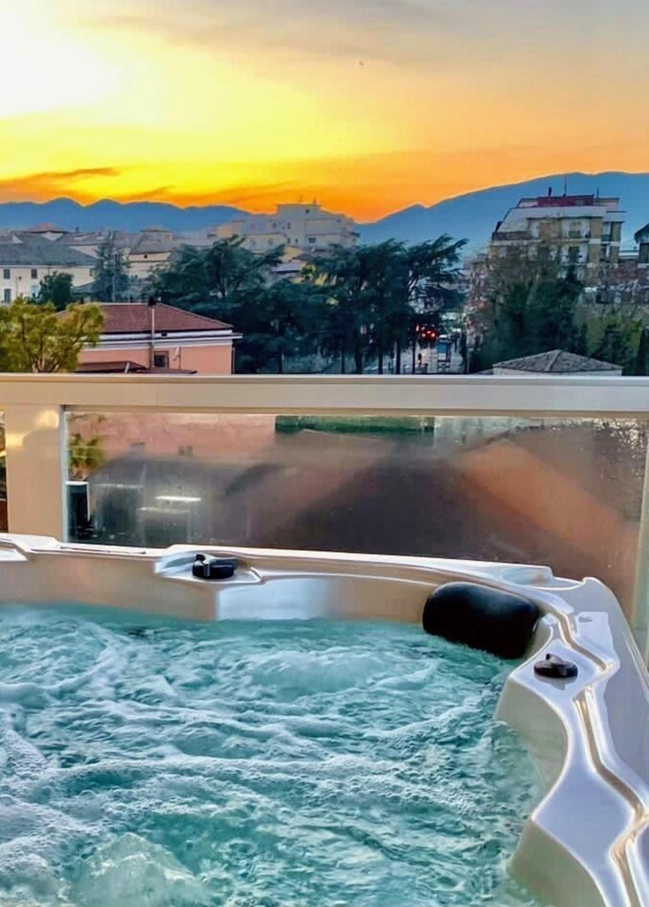 Una vasca idromassaggio con vista sulle montagne e sugli edifici al tramonto.