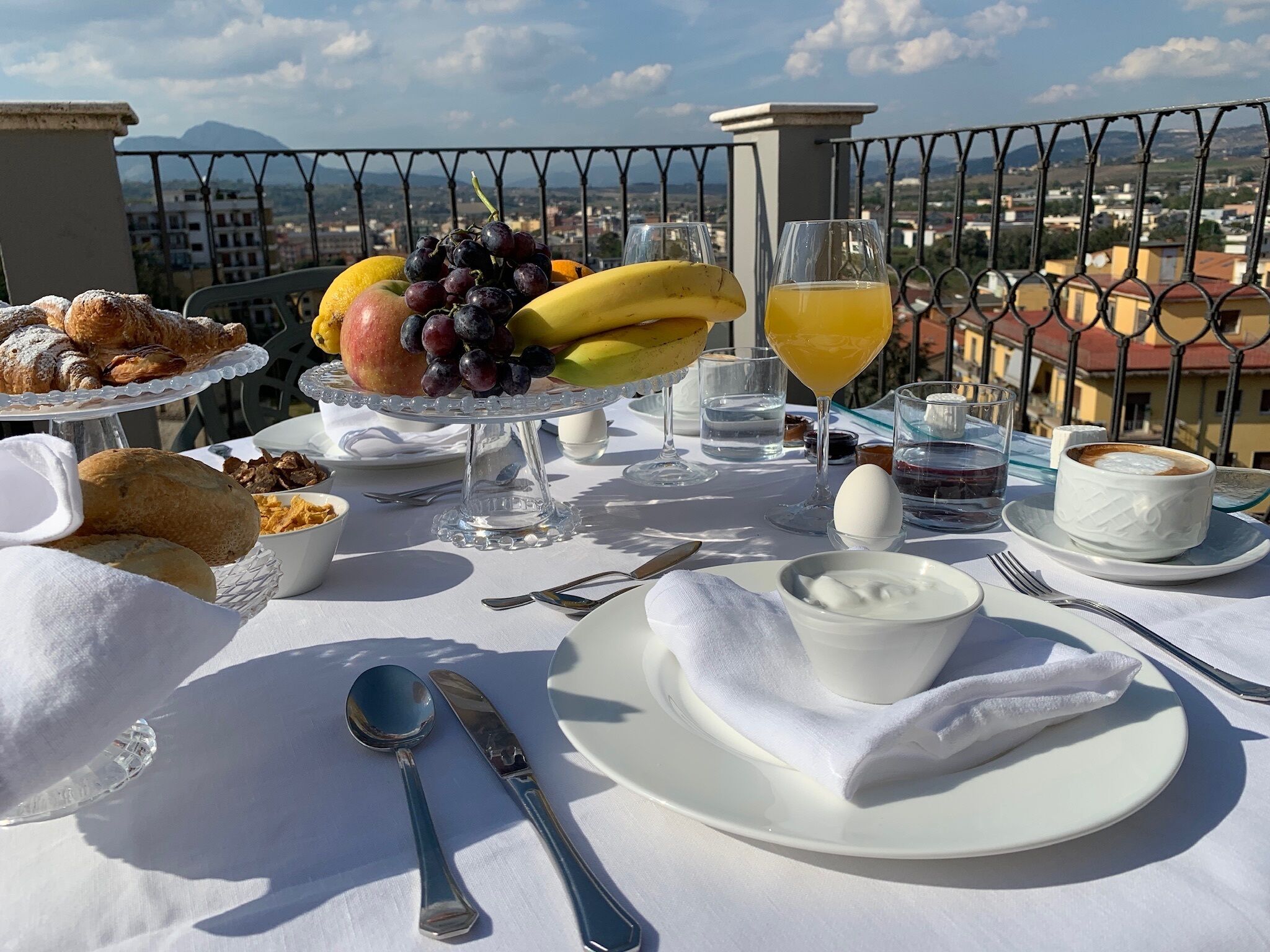A breakfast setup on a balcony with a view of the city and mountains.