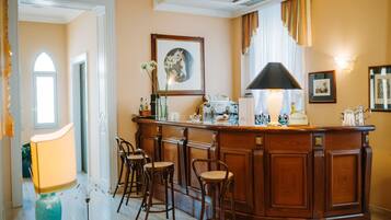 A bar area with a wooden counter, bar stools, a framed picture, and a lamp.