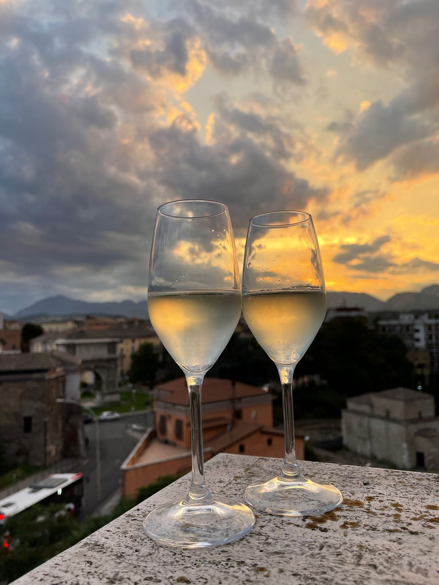 Deux verres de vin blanc sur un balcon, avec une vue sur la ville et des montagnes en arrière-plan.