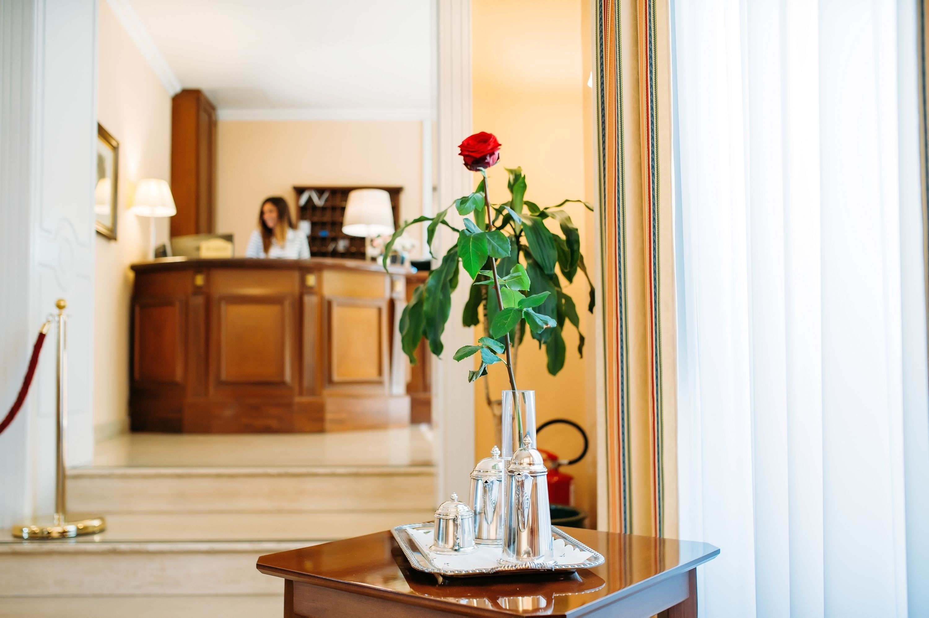 A reception area with a desk, a red rose in a vase, and a tray with silver items.