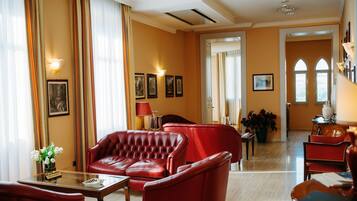 Un hall d’hôtel avec des canapés en cuir rouge, une table basse en verre et un lustre.