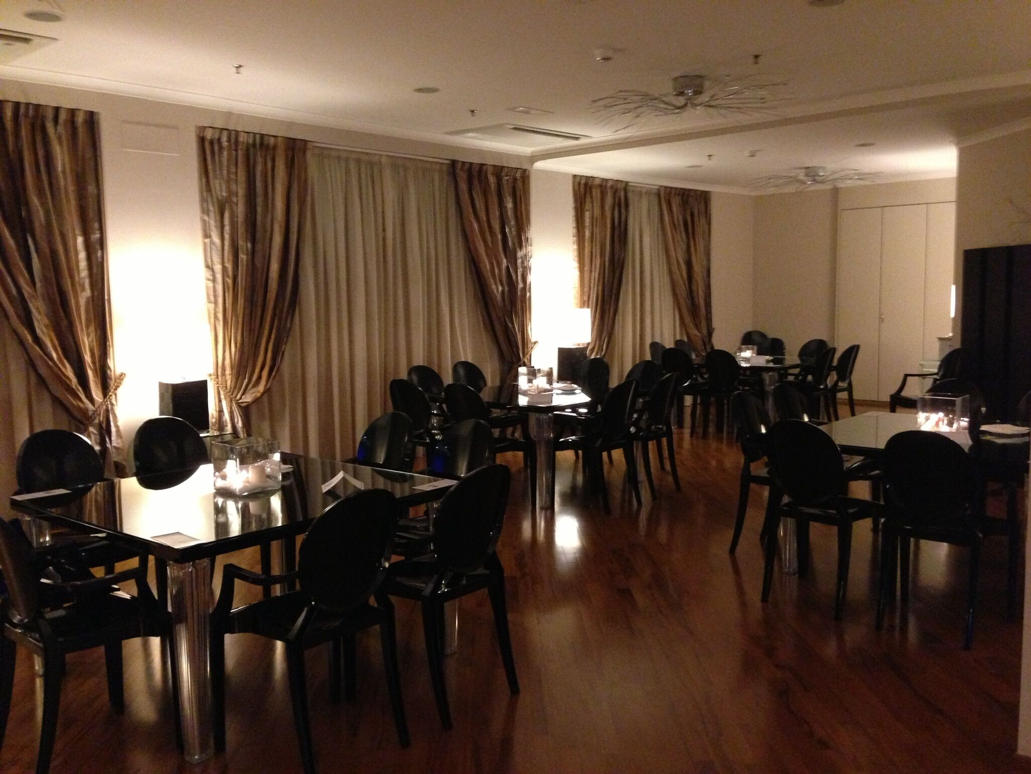 A conference room with multiple tables and chairs, large windows with curtains, and a ceiling fan.