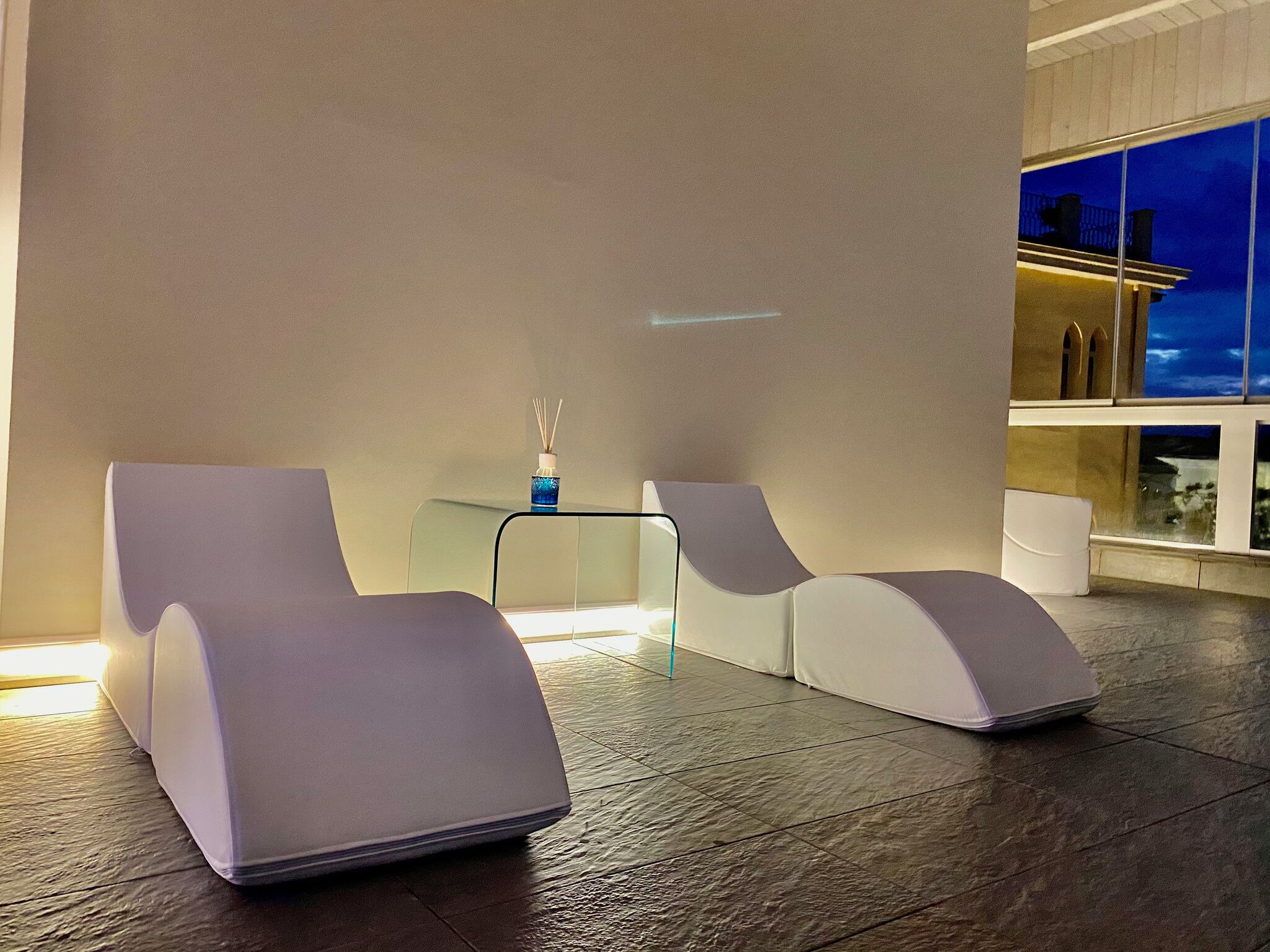 Un área de descanso moderna con dos sillones blancos y una mesita con un jarrón azul.