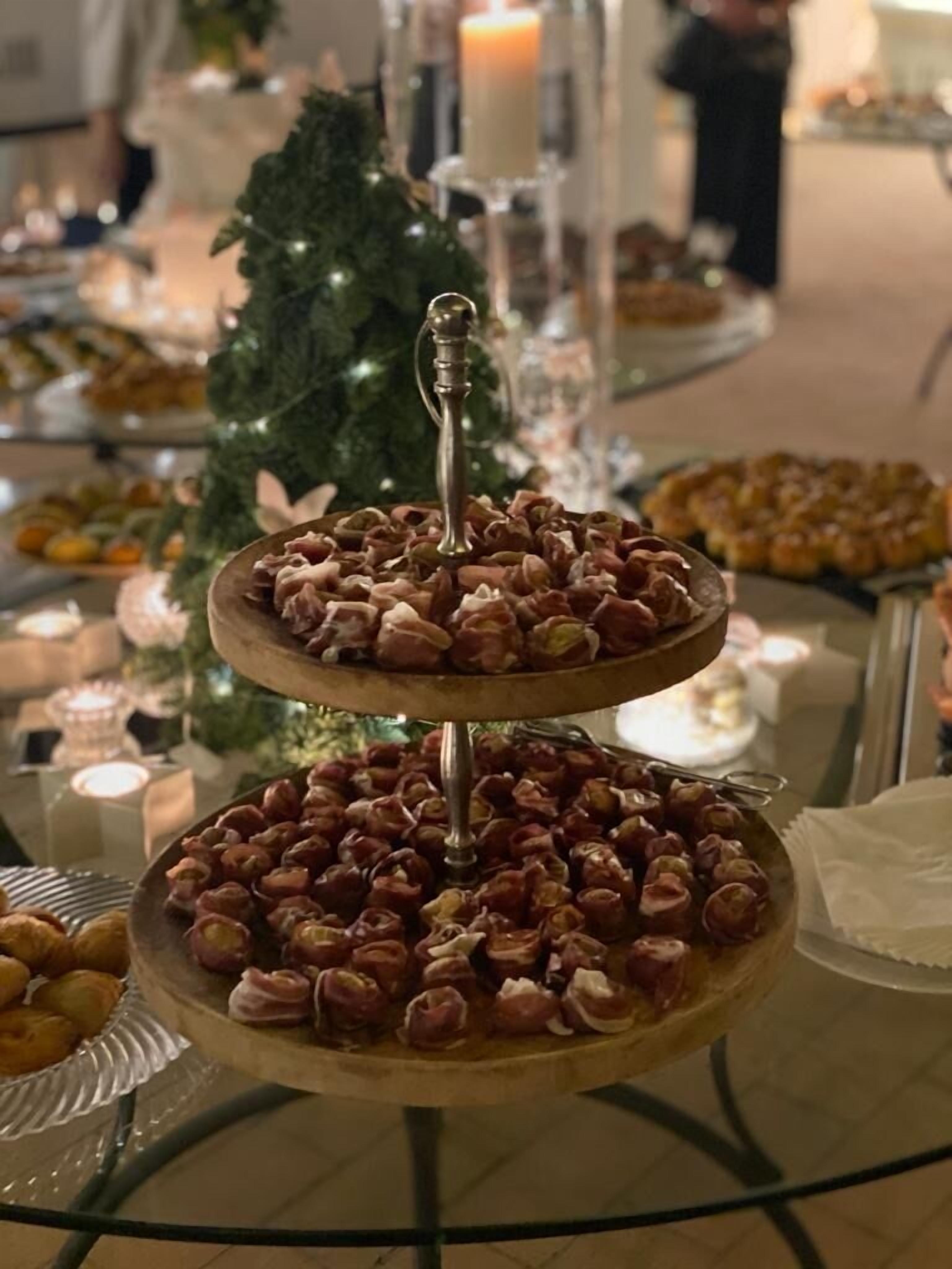 A multi-tiered dessert stand with various pastries, a Christmas tree, and candles in the background.