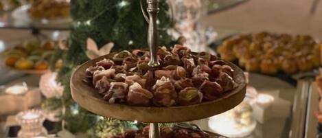 A multi-tiered dessert stand with various pastries, a Christmas tree, and candles in the background.