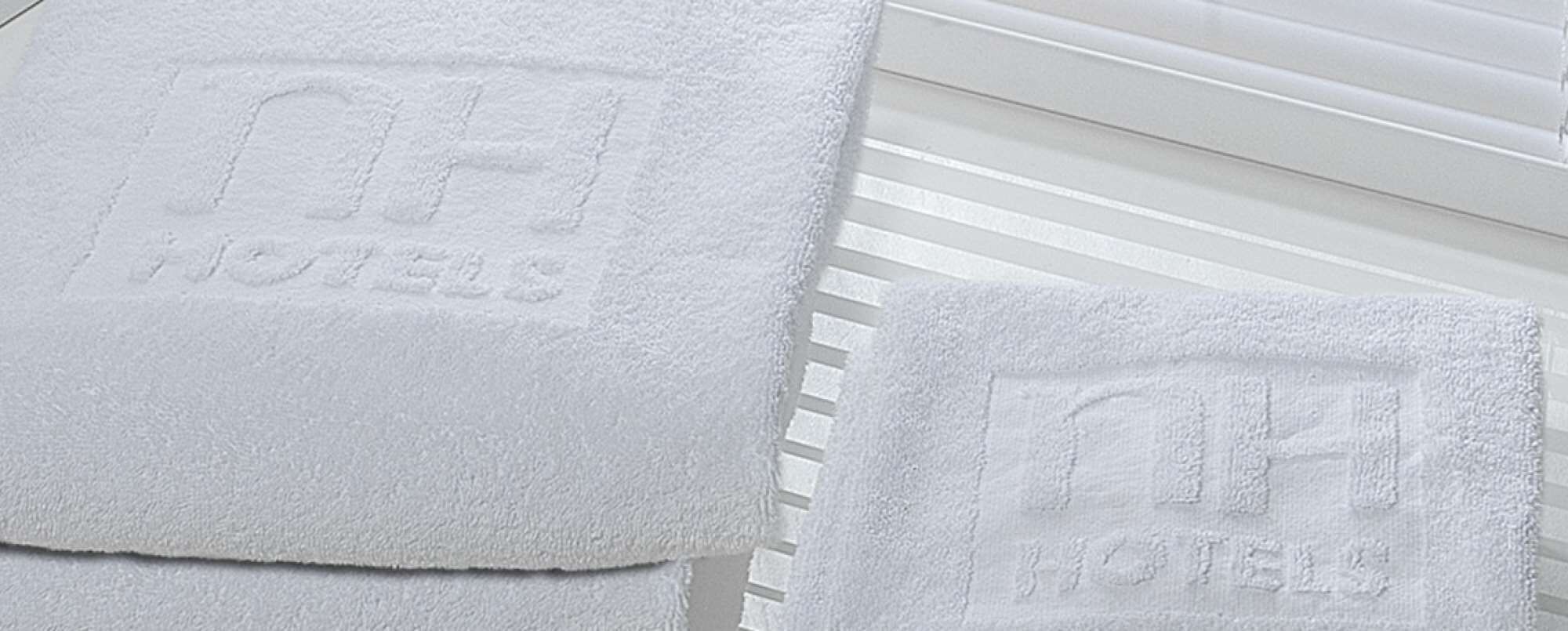Deux serviettes blanches ornées d’un motif en relief, posées sur une surface blanche à rayures horizontales.