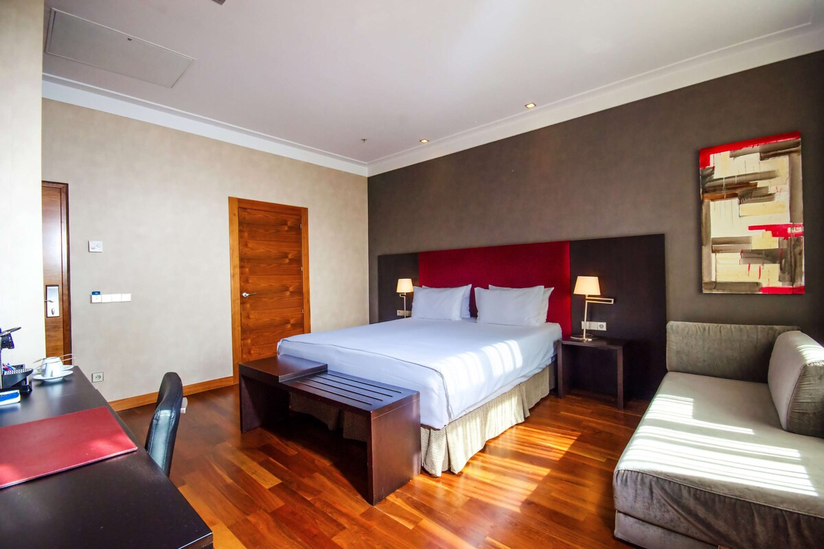 Une chambre d’hôtel comprenant un lit, un bureau, une chaise, un canapé et une table de chevet avec une lampe.