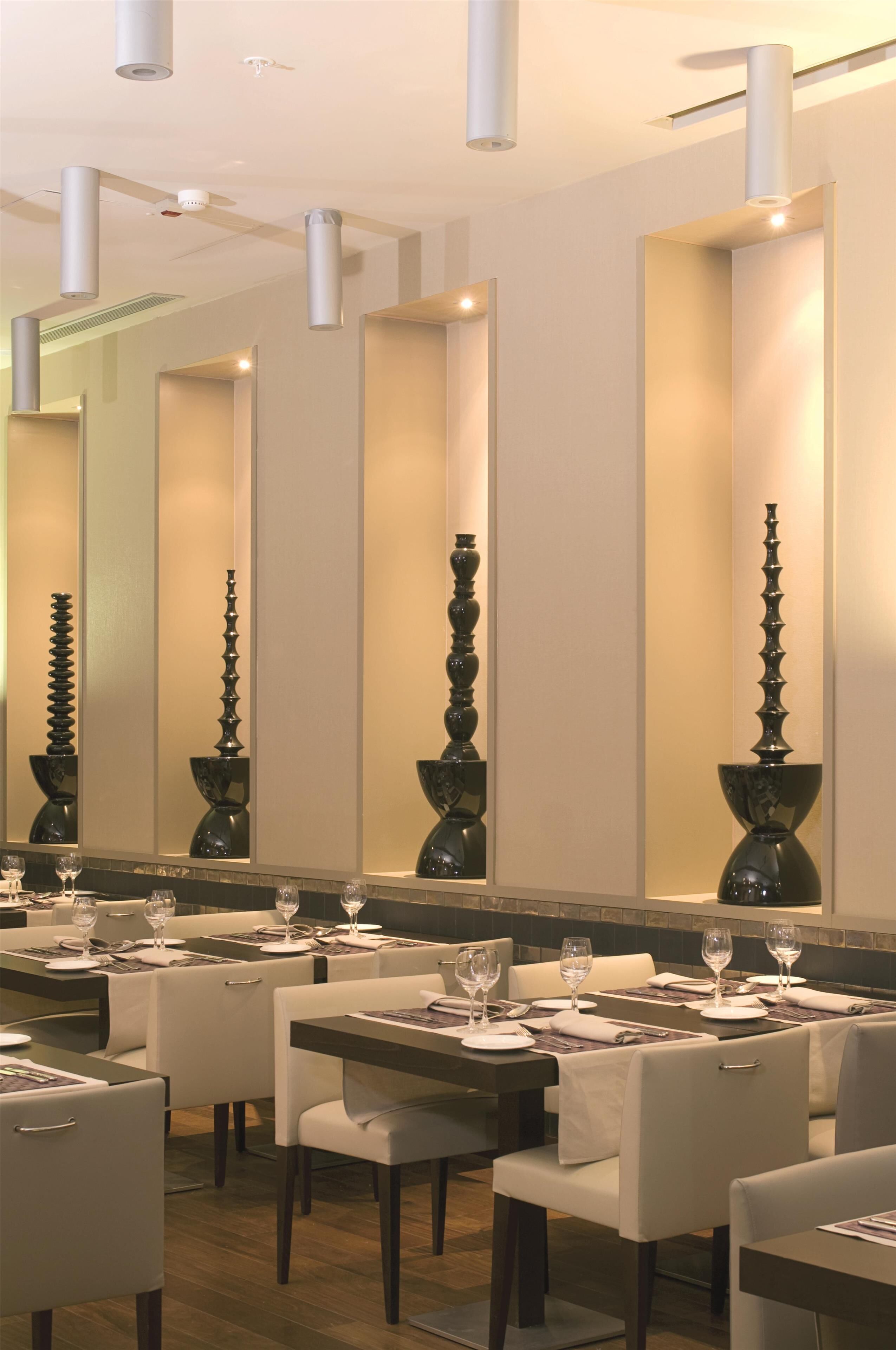 A restaurant with tables set for dining, a large mirror on the wall, and decorative vases.