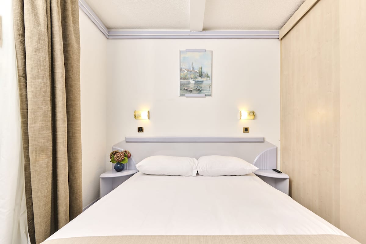 Siististi pedattu sänky hotellihuoneessa, jossa on pääty, yöpöytävalaisimet ja taulu seinällä.