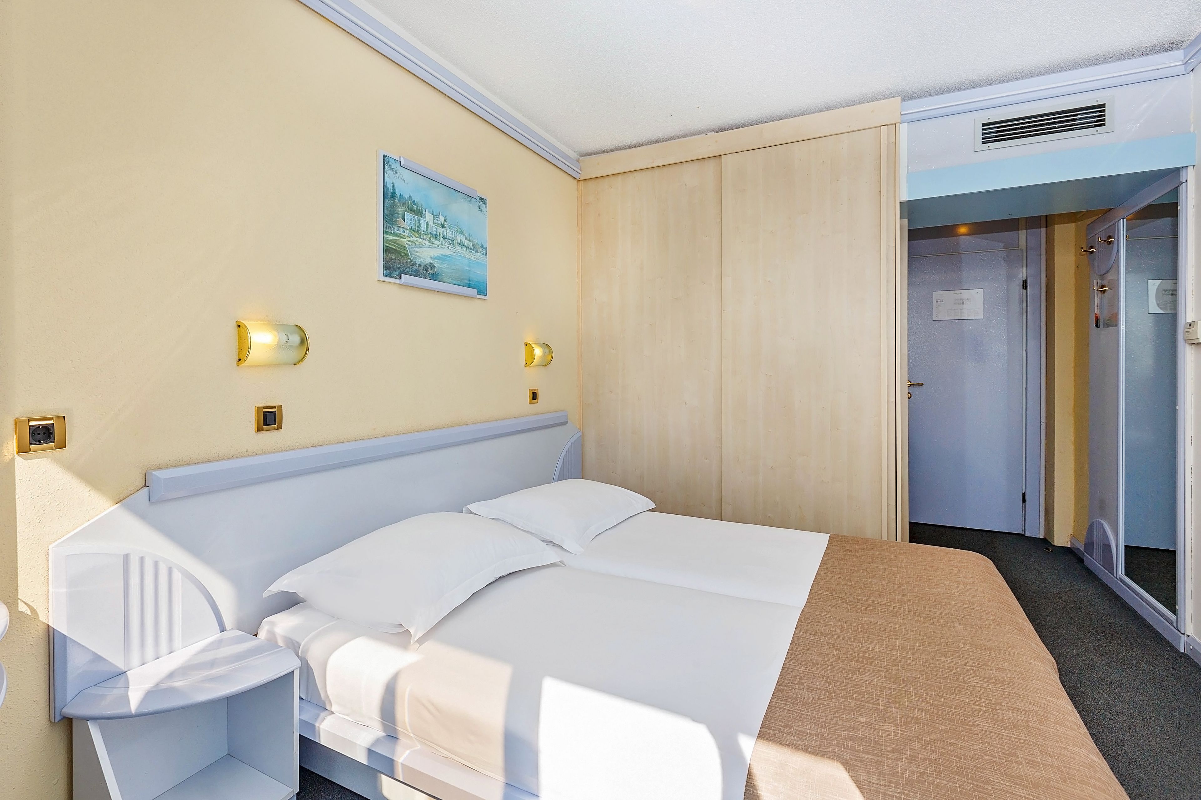 Une chambre d’hôtel avec un lit, des tables de chevet, un tableau au mur et une armoire.