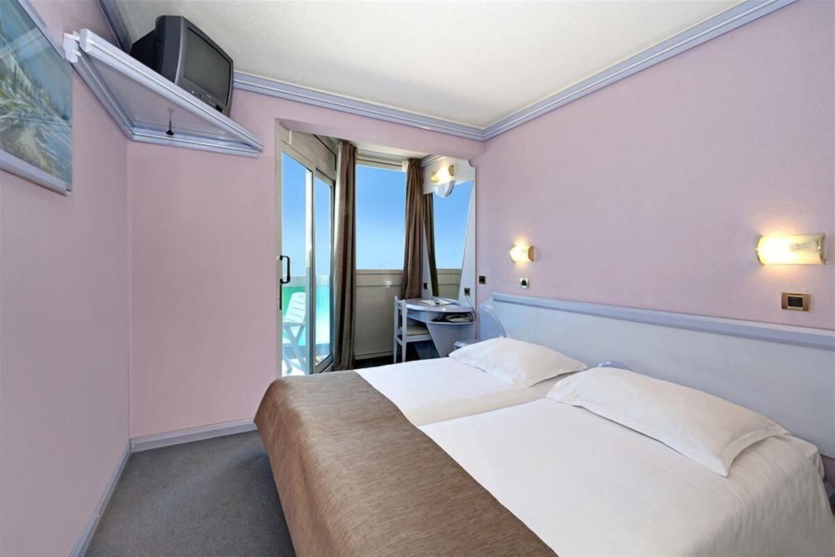 A hotel room with a bed, a desk, a chair, a television, and a window with curtains.