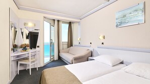Una habitación de hotel con cama, escritorio, silla, mesita de noche, lámpara, un cuadro y vistas al mar.