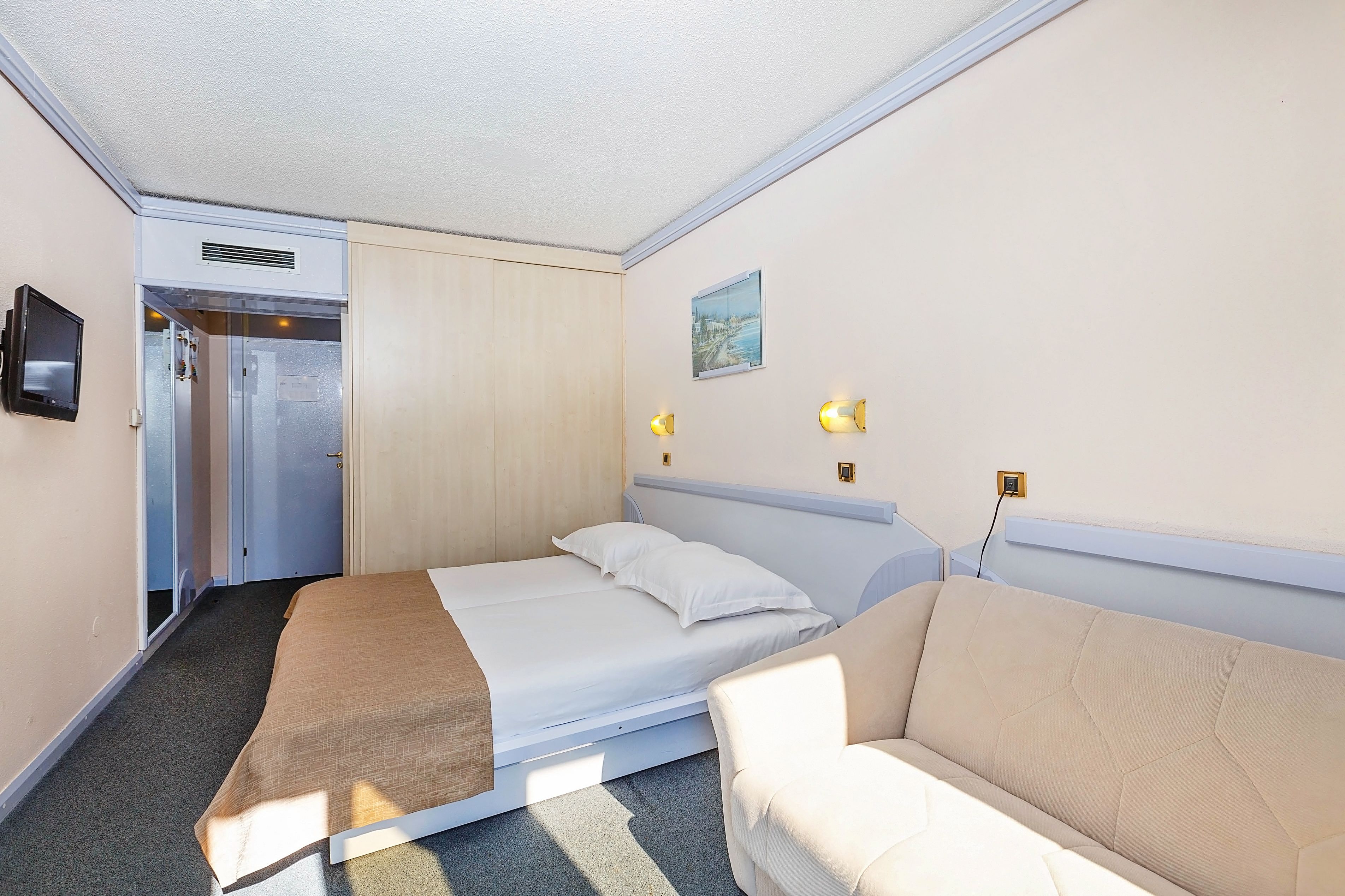 A hotel room with a bed, a sofa, a TV, and a painting on the wall.
