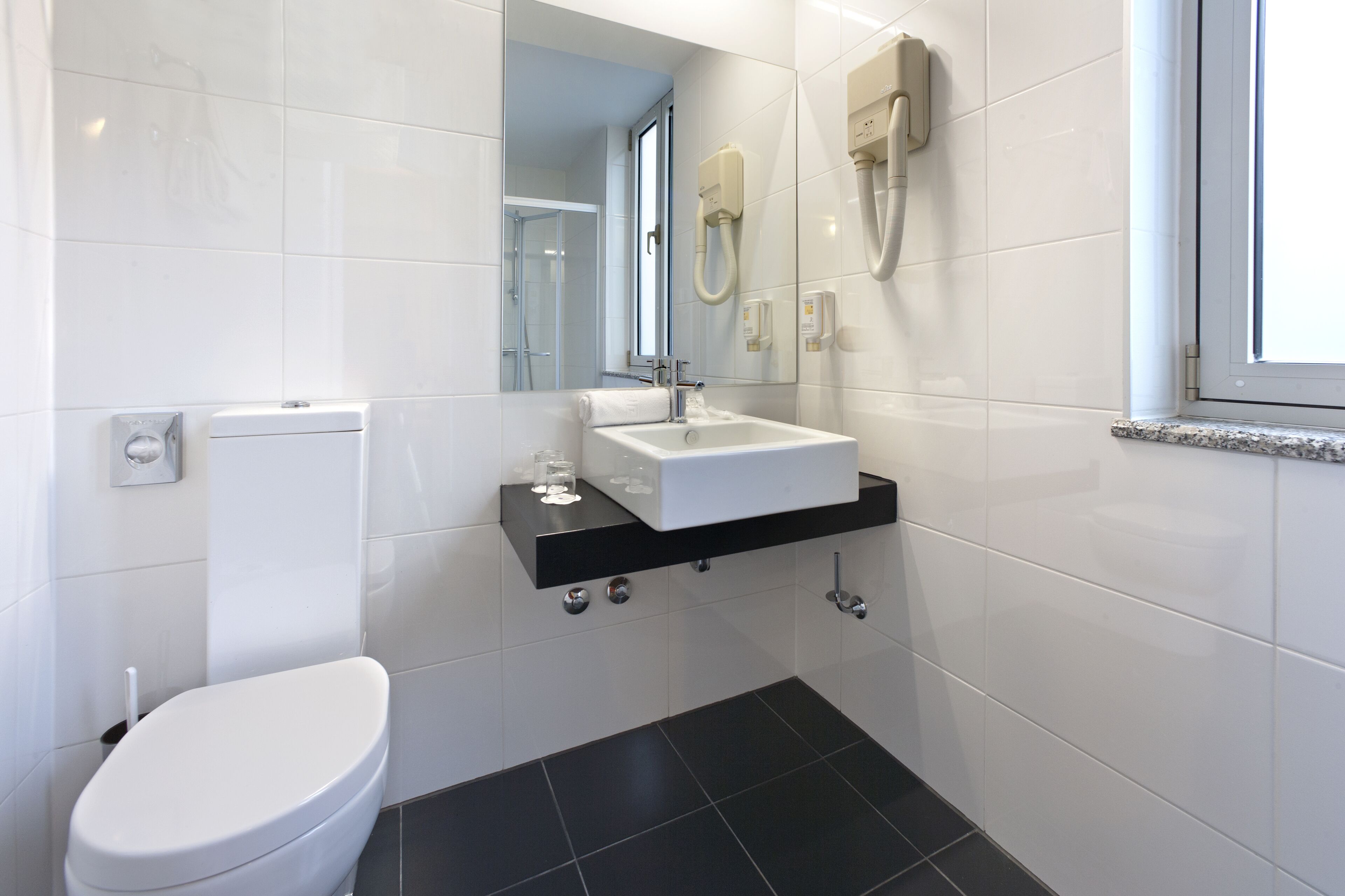 Ein modernes Badezimmer mit Toilette in Weiß, einem schwarzen Waschbecken und einem Spiegel darüber.