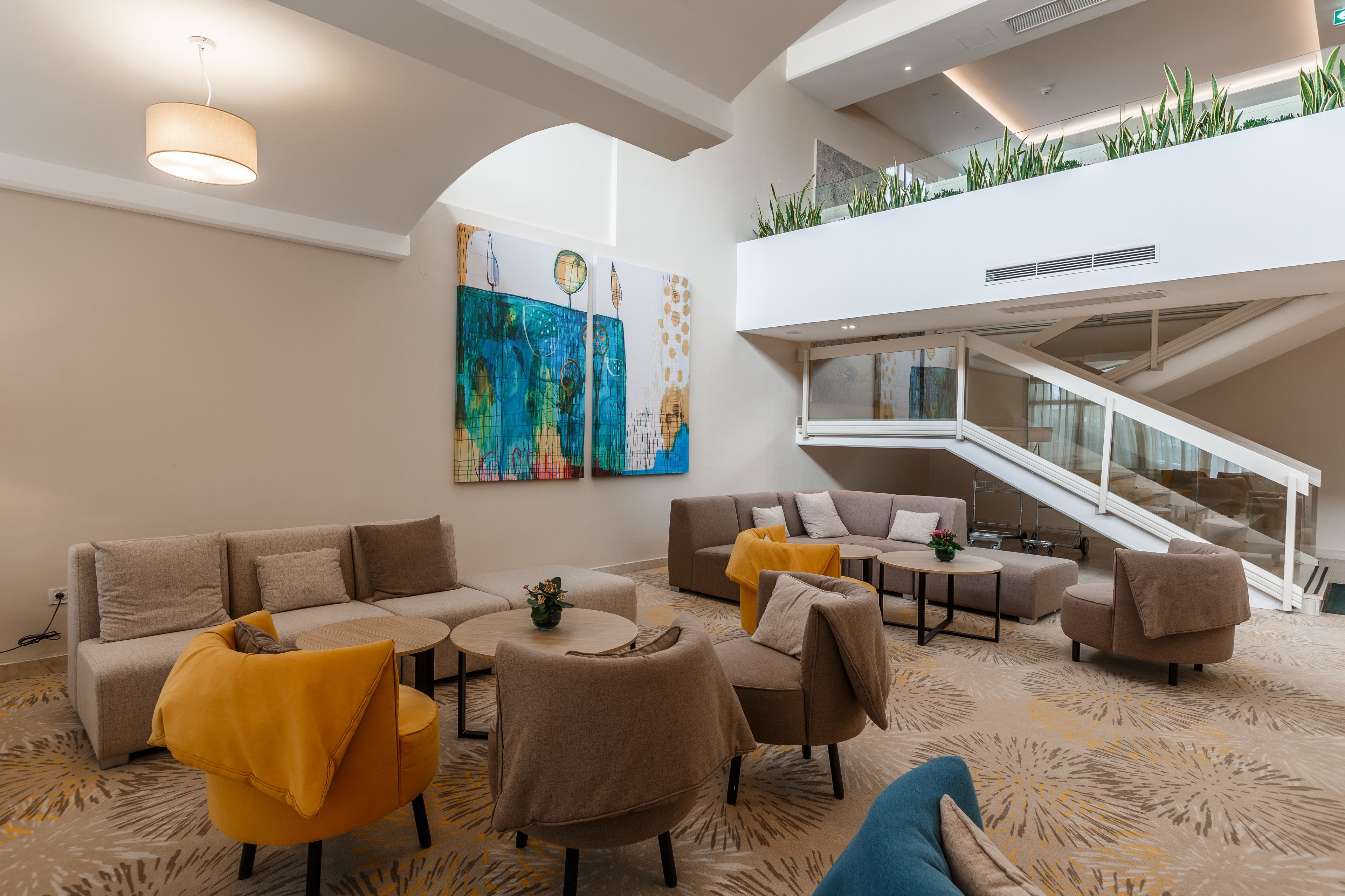 A modern lobby with a high ceiling, a staircase, and a large abstract painting.