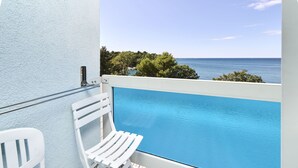 Zona junto a la piscina con una silla blanca y una barrera de cristal con vistas al mar.