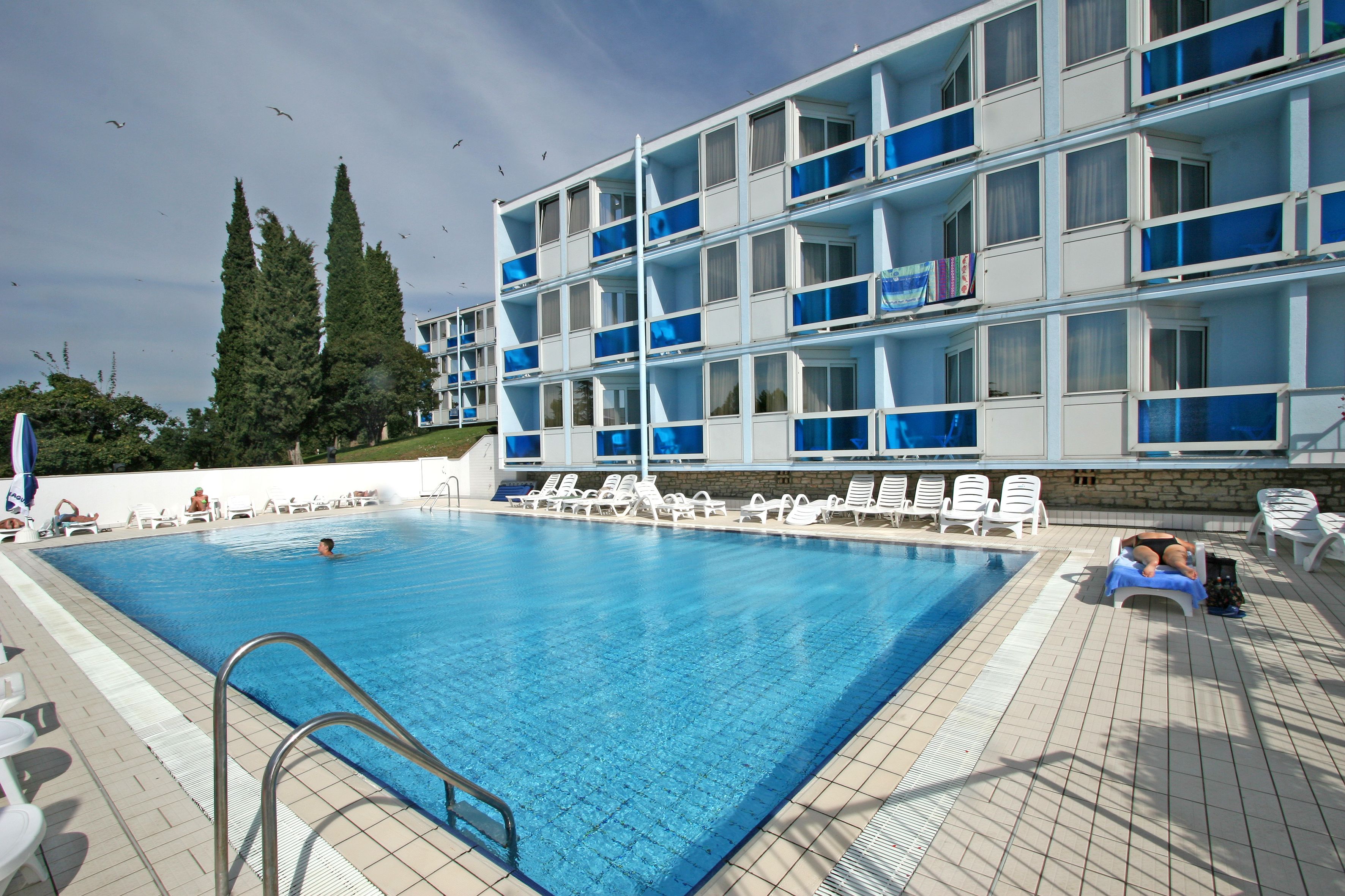 A swimming pool with lounge chairs and a building with multiple balconies.