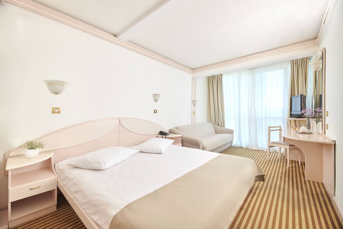 A hotel room with a large bed, a desk, a chair, a television, and a window with curtains.
