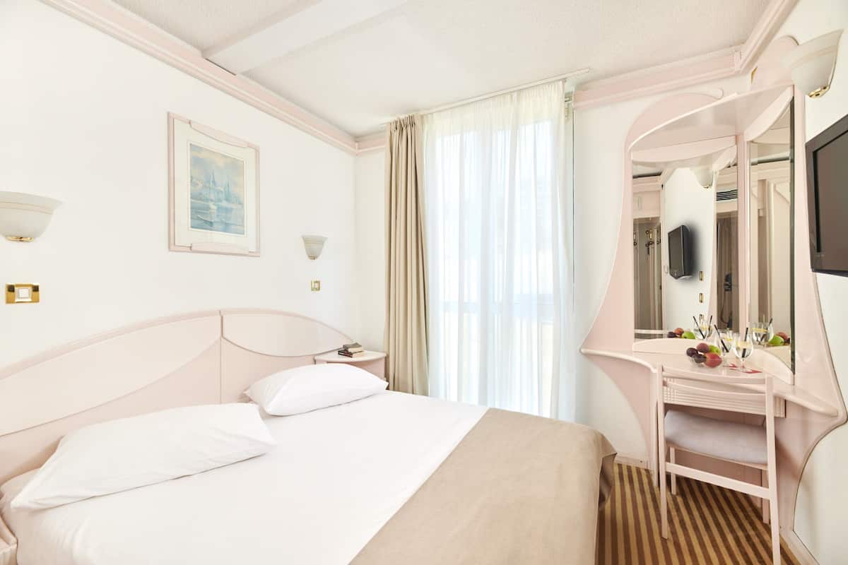 A hotel room with a bed, bedside table, and a vanity with a mirror.