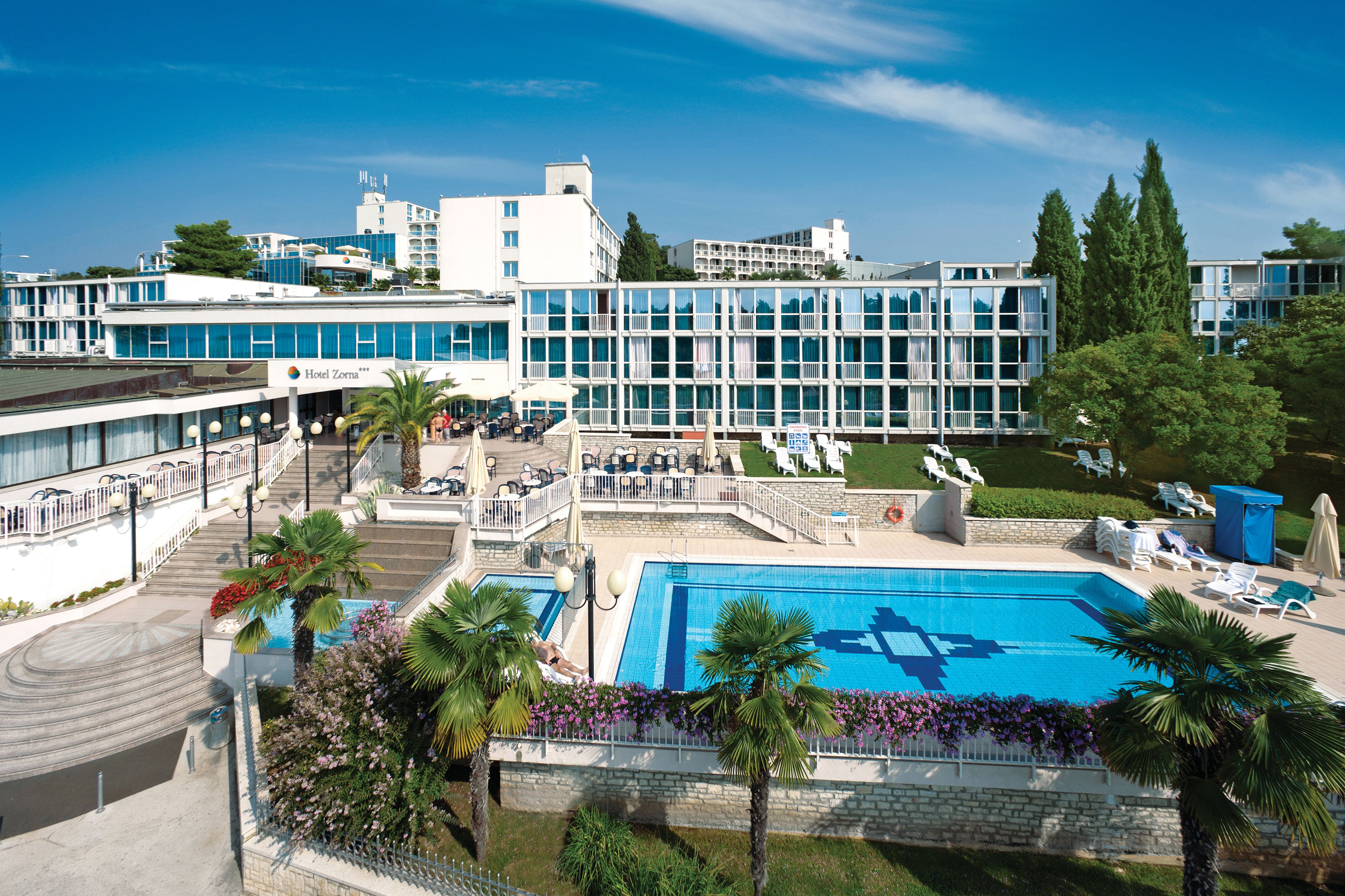 A hotel with a swimming pool, outdoor seating, and a view of the surrounding buildings.