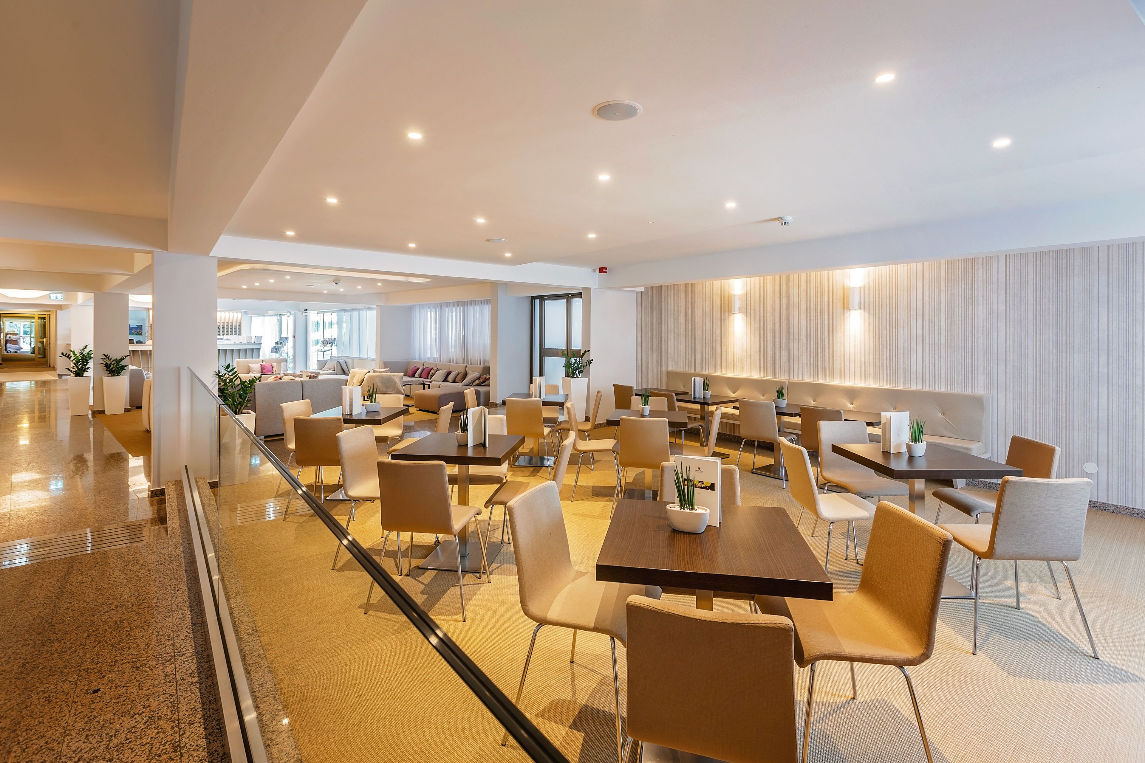 A spacious, well-lit dining area with multiple tables and chairs, a modern interior design, and a view of the adjacent living area.