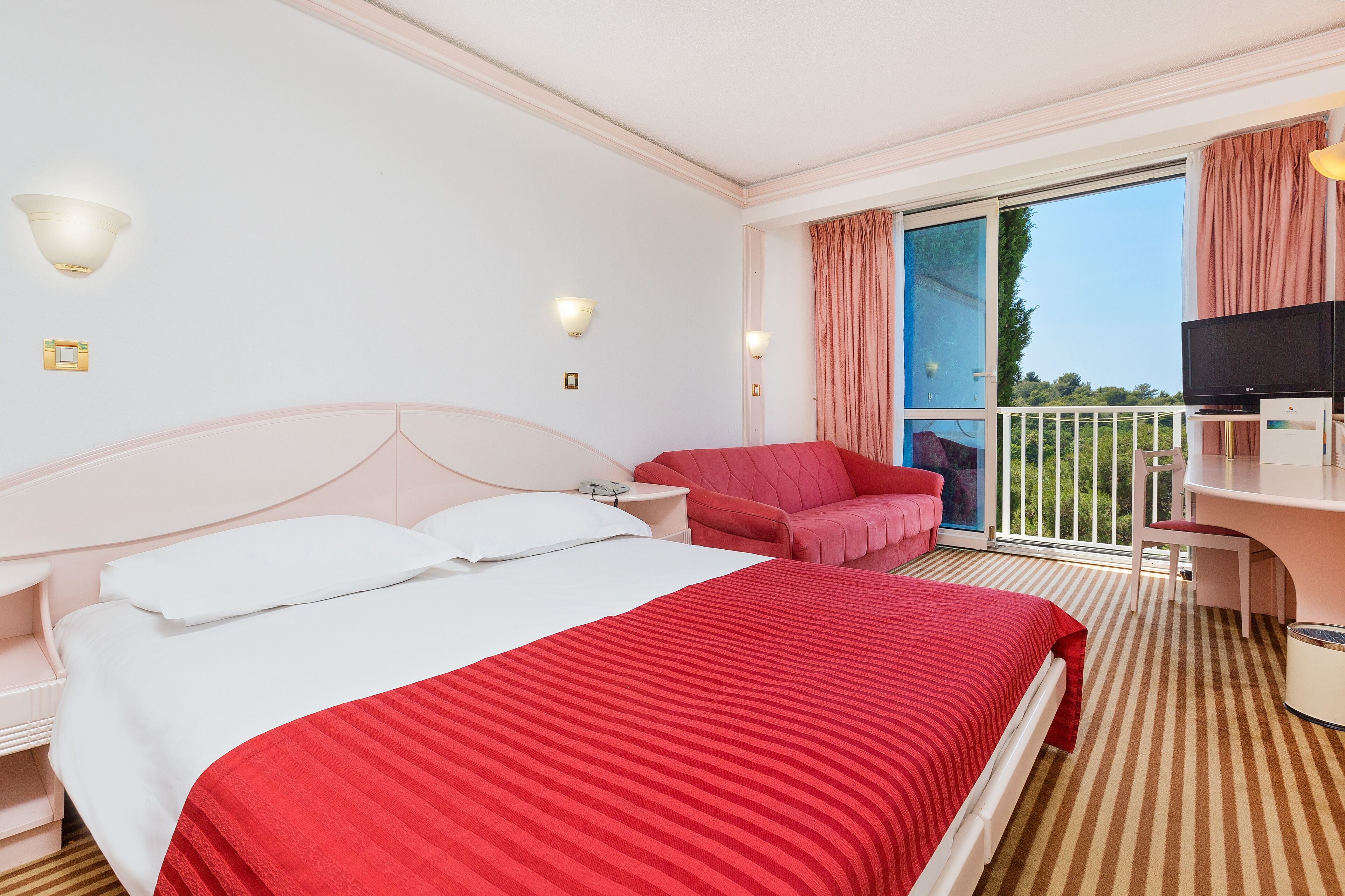 A hotel room with a large bed, a desk, a chair, and a balcony with a view.