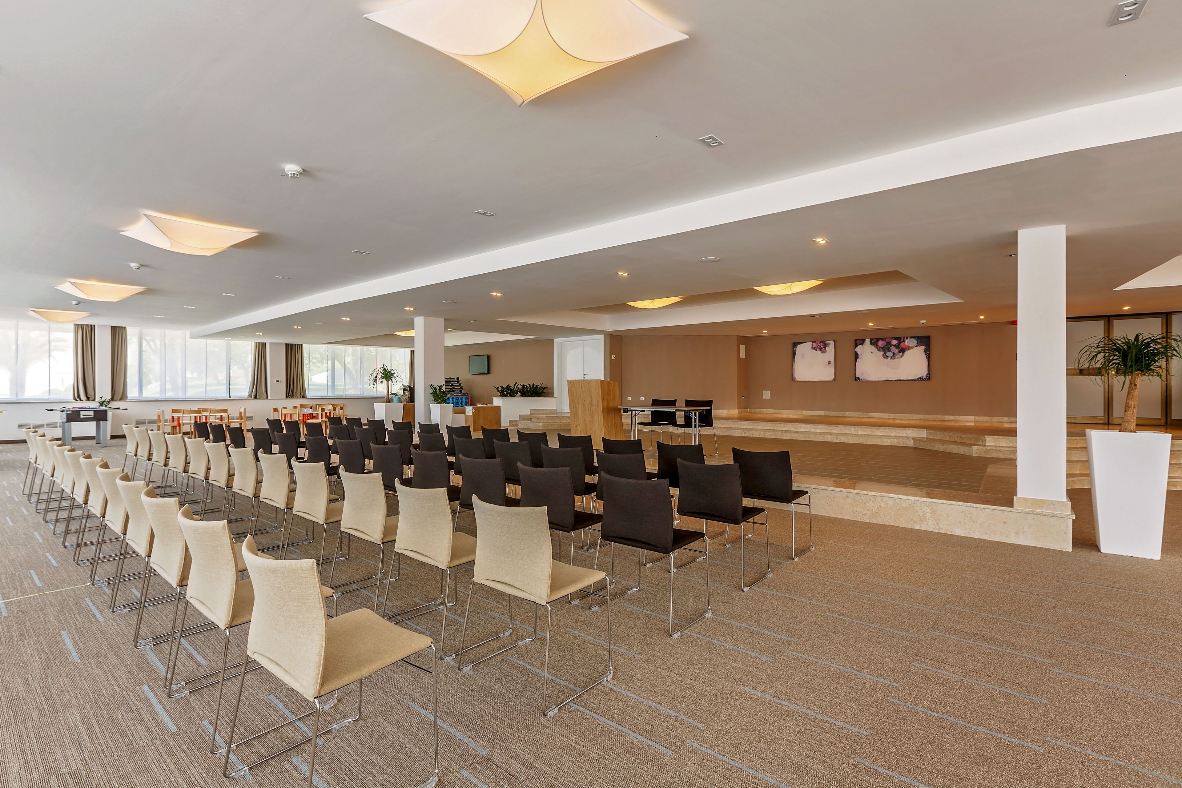 A spacious conference room with rows of chairs, a stage, and a modern ceiling design.