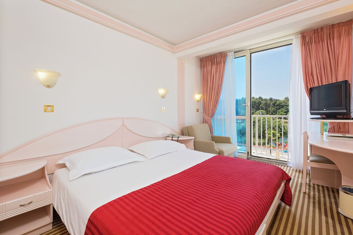 A hotel room with a bed, a desk, a television, and a balcony with a view of the outdoors.