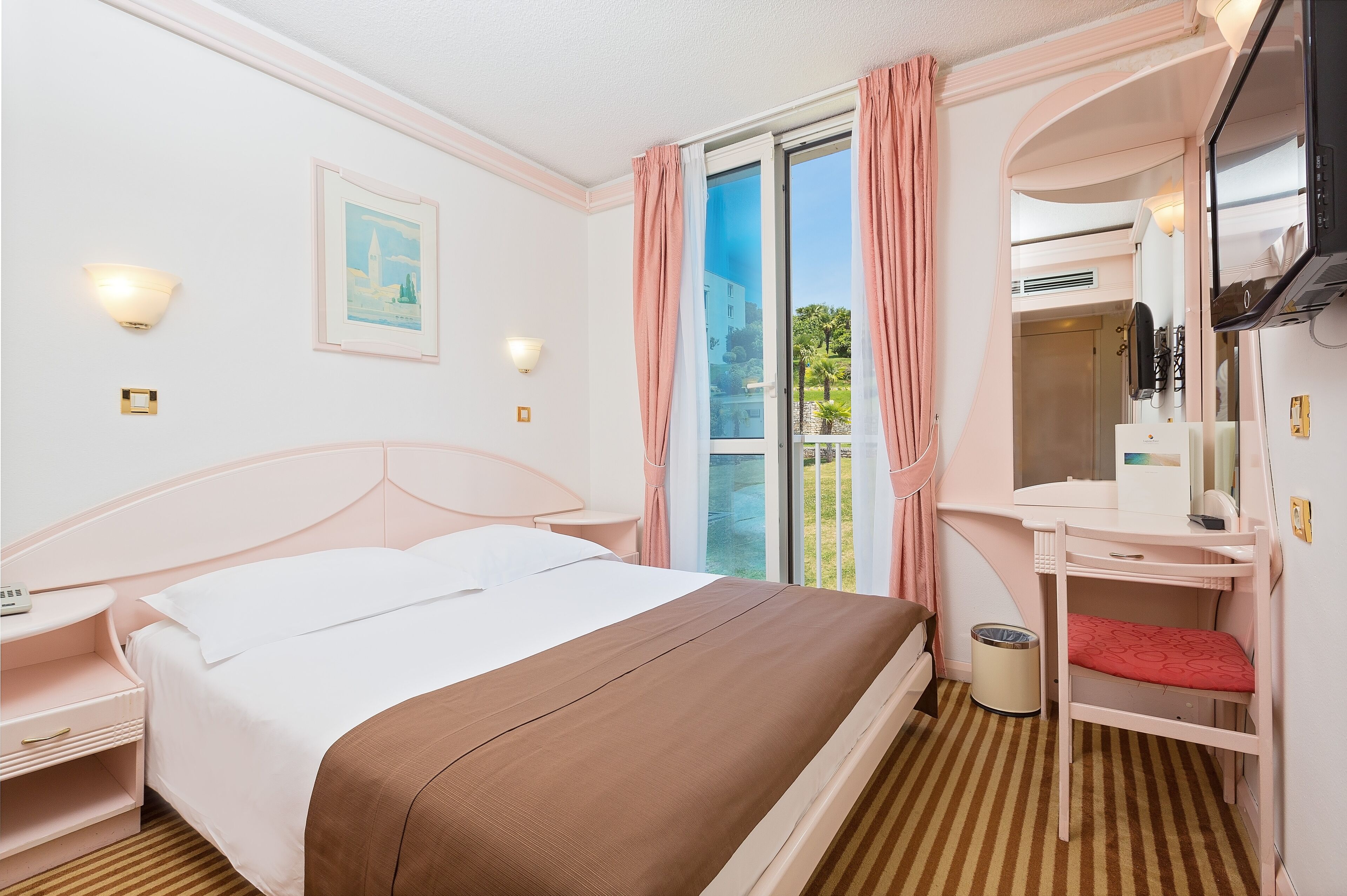 A hotel room with a bed, a desk with a chair, a TV, and a window with curtains.