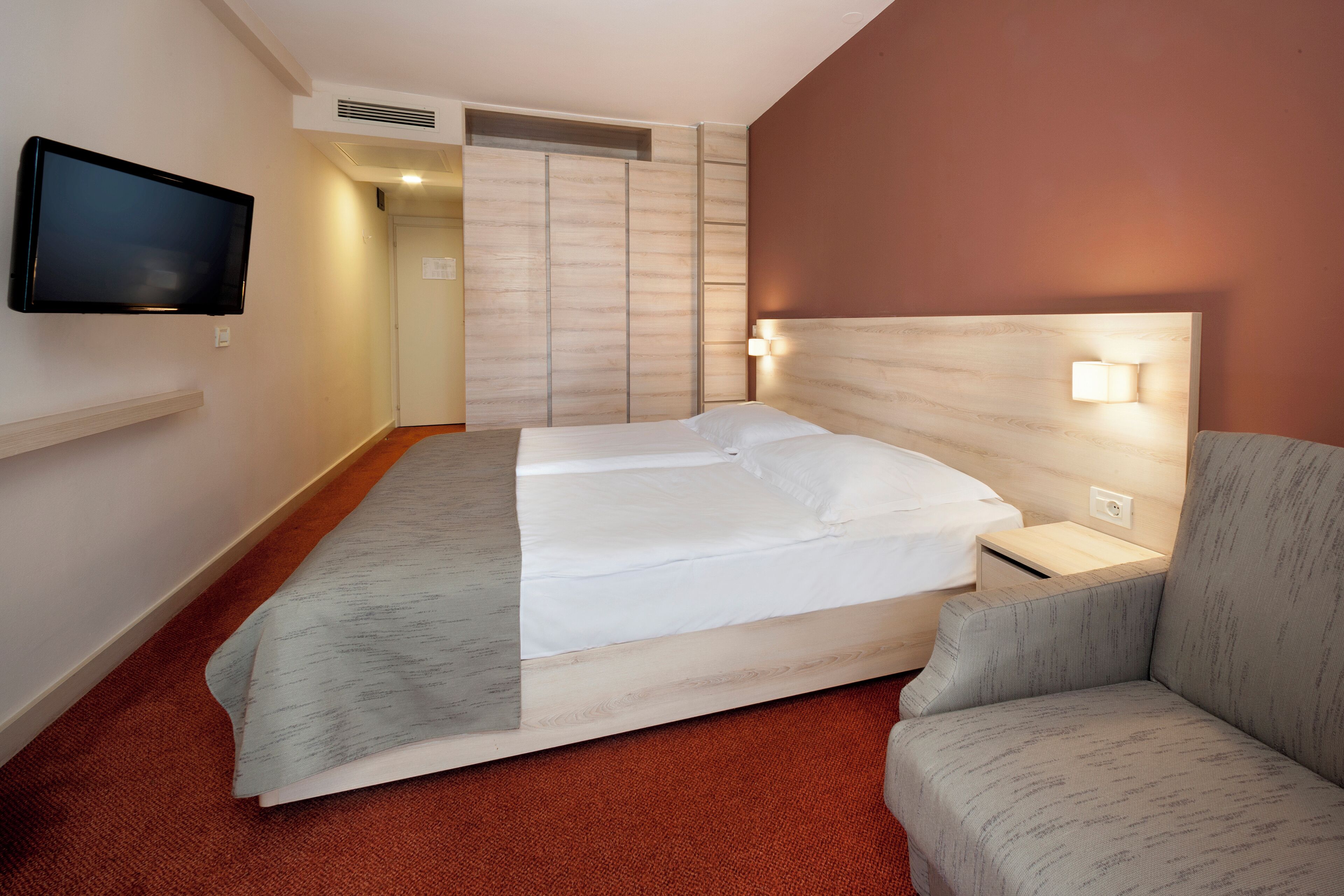 Habitación de hotel con una cama, televisión, mesita de noche y una lámpara en la pared.
