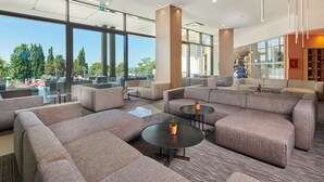 Un área de descanso moderna con sofás y mesas, ventanas amplias que ofrecen vistas al exterior, y una estantería al fondo.