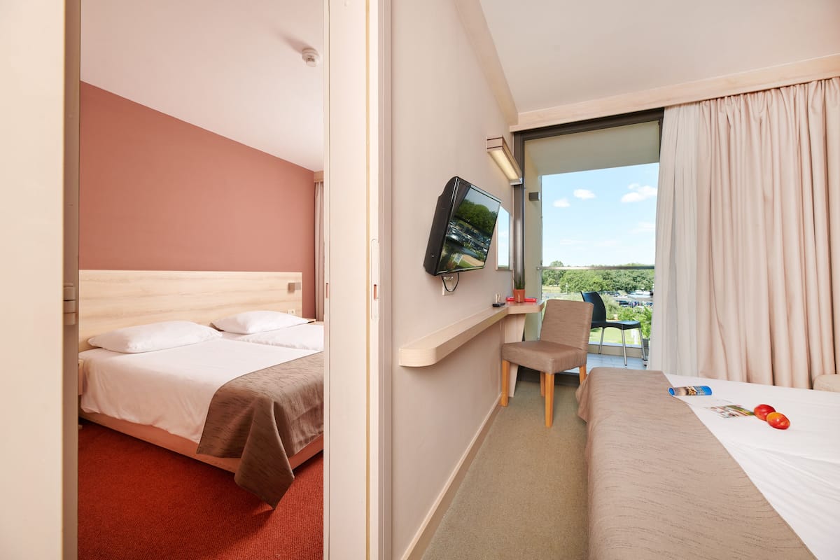 A hotel room with a bed, a desk with a chair, a television, and a window with curtains.