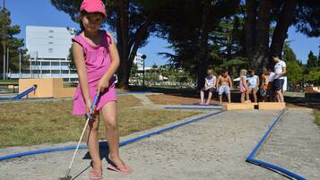 A young girl playing croquet in a park with trees and a building in the background.