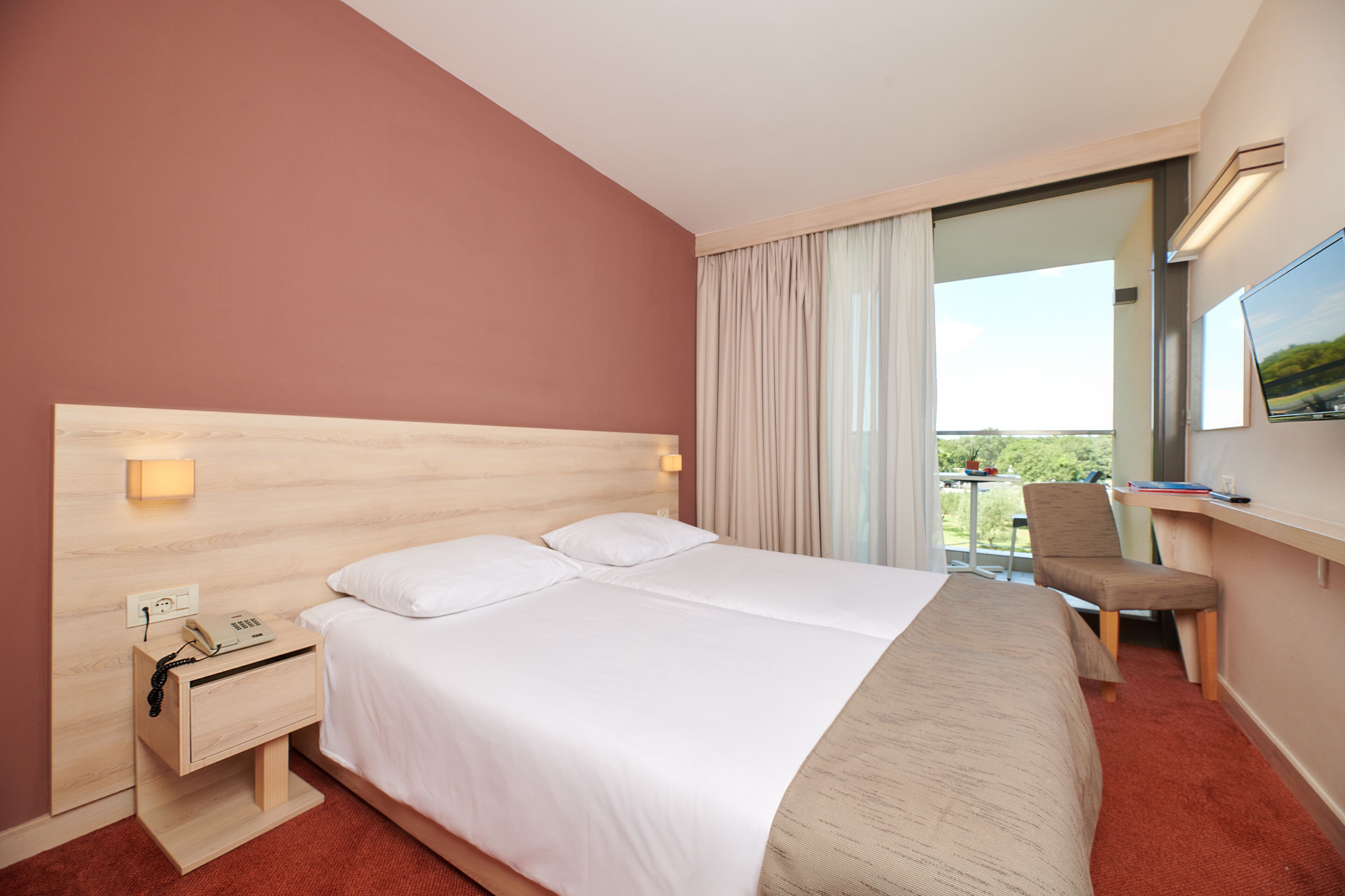 A hotel room with a large bed, a desk with a chair, a TV, and a window with curtains.